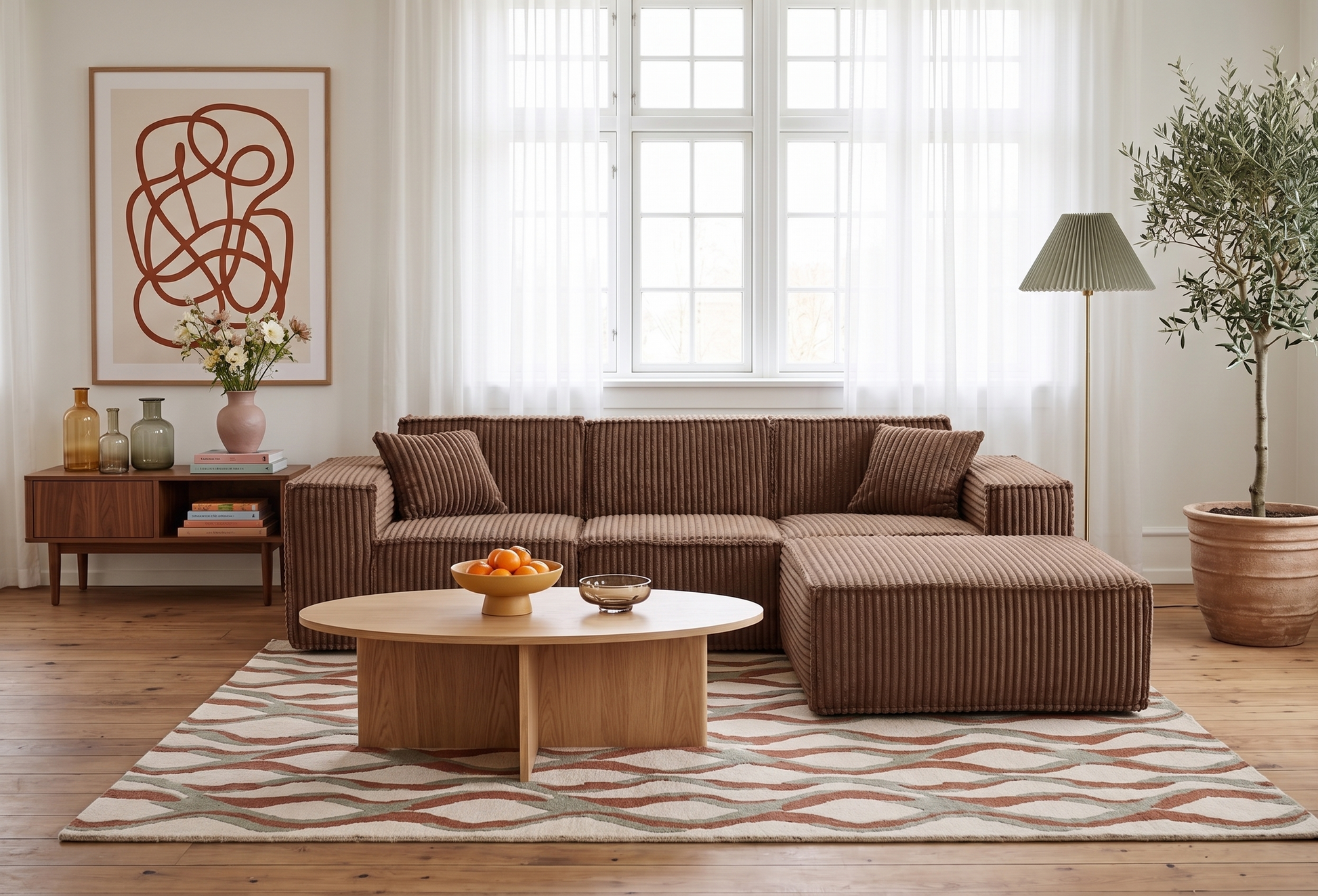 A brown corduroy sectional sofa with a chaise lounge in a bright, modern living room. The sofa is styled with matching throw pillows, set on a patterned area rug with a light wood coffee table in front.